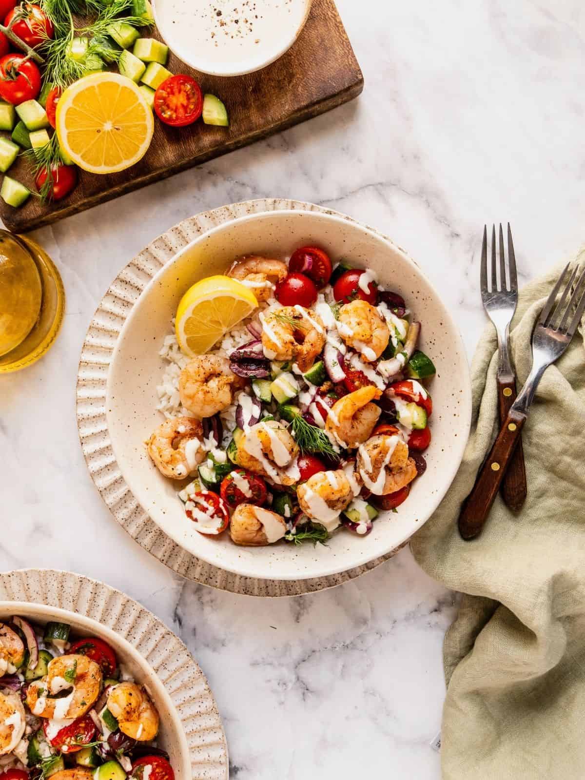 Mediterranean shrimp rice bowl with chopped cucumber, tomatoes, olives garnished with fresh dill.