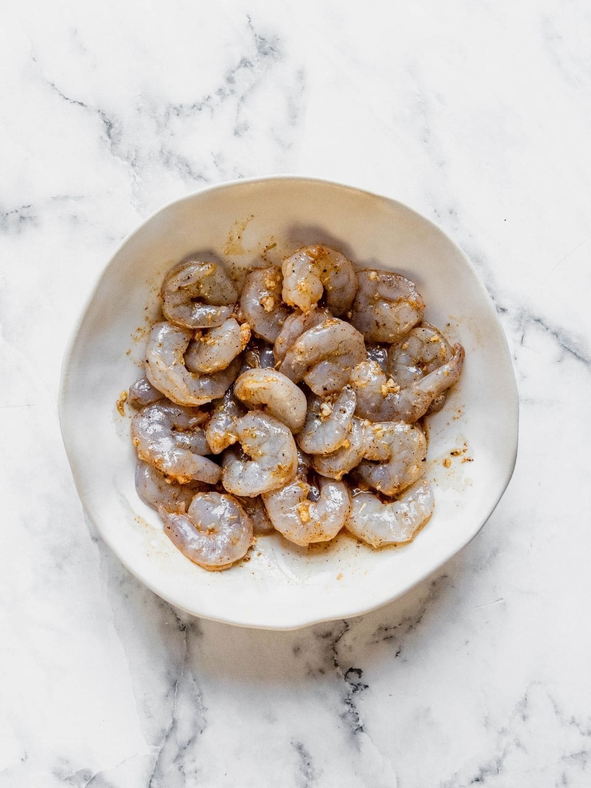Shrimp marinating in a bowl with seasoning, olive oil and garlic.