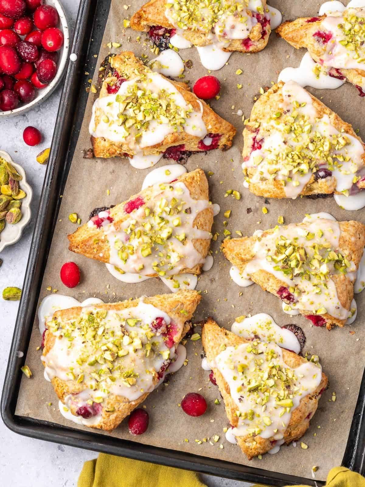 Pistachio and Cranberry Scones garnished with icing and crushed pistachios on a baking tray.