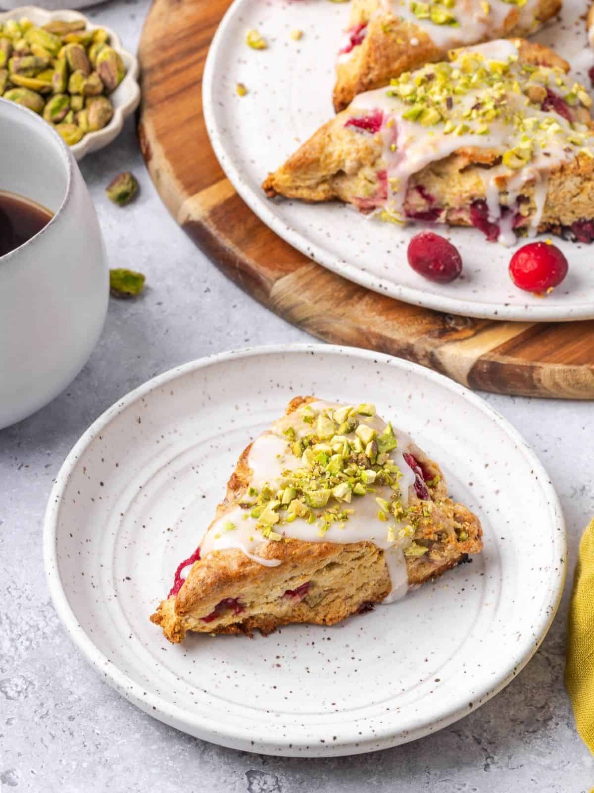 Pistachio Cranberry Scones garnished with icing and crushed pistachios on a plate.