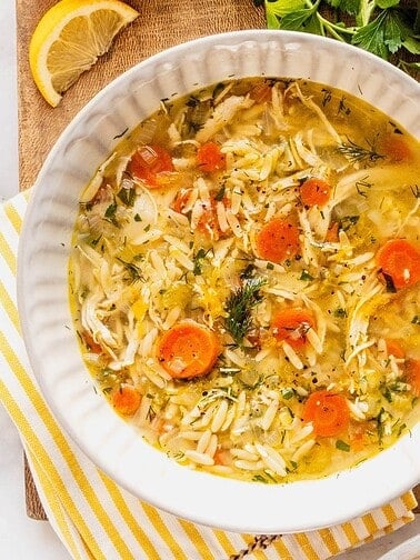 Bowl with chicken, orzo and carrot soup on a wooden tray.