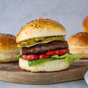A hamburger with lettuce, tomatoes an cheese on a wooden board.