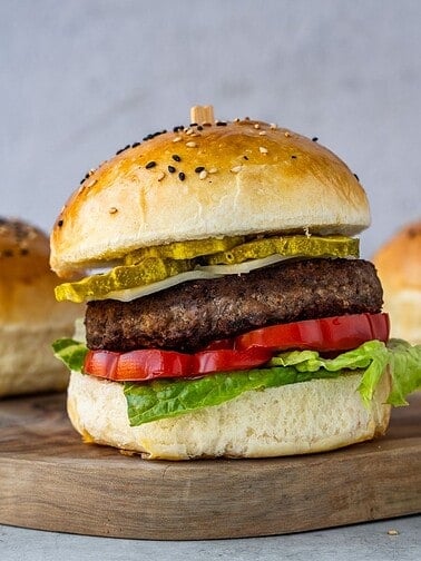 A hamburger with lettuce, tomatoes an cheese on a wooden board.
