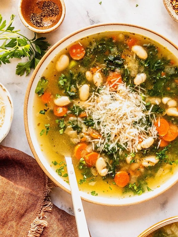 Tuscan white bean soup with kale in a bowl garnished with fresh herbs and shaved parmesan.