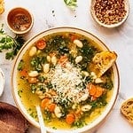 Tuscan white bean soup with kale in a bowl garnished with fresh herbs and shaved parmesan.
