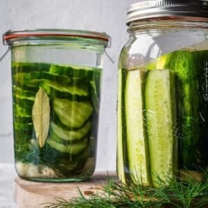 Two mason jars filled with sliced cucumbers with pickling brine and spices.