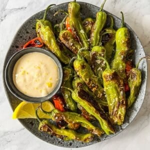 Plate with blistered shishito peppers with a side of tahini sauce.