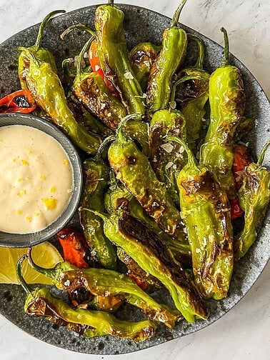 Plate with blistered shishito peppers with a side of tahini sauce.