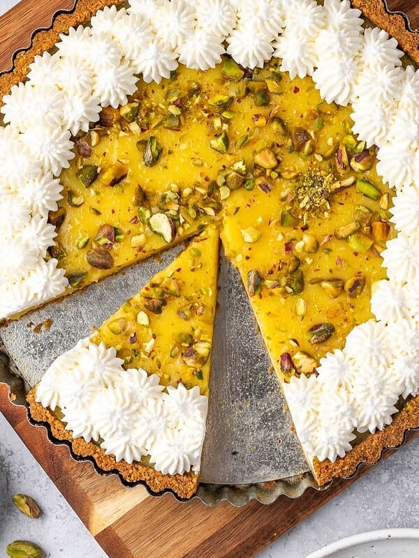 Lemon curd tart with pistachios decorated with piped whipped cream.