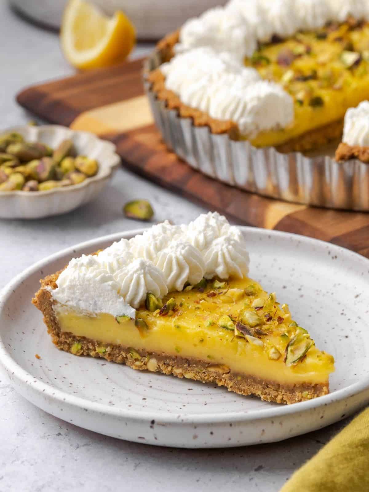 A slice of lemon curd tart with pistachios, decorated with piped whipped cream.