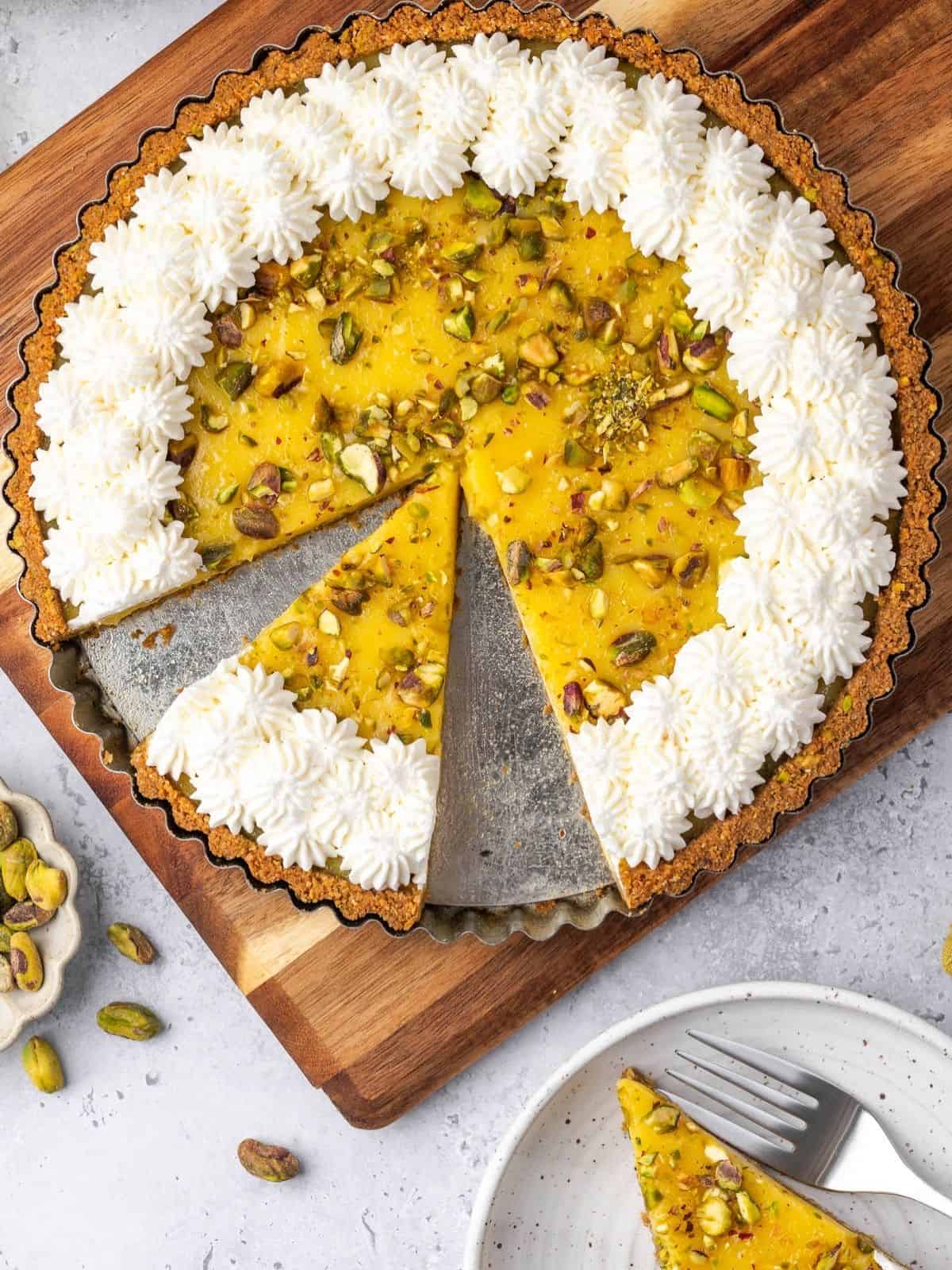Lemon curd tart with pistachios, decorated with piped whipped cream.