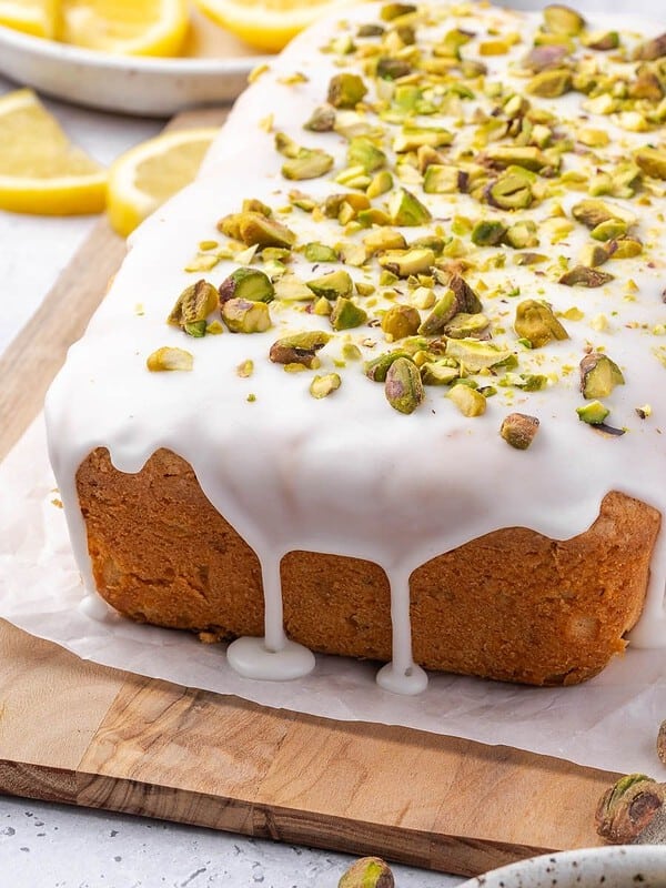 Lemon pistachio pound cake drizzled with lemon icing and decorated with crushed pistachios on a wooden board.