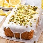 Lemon pistachio pound cake drizzled with lemon icing and decorated with crushed pistachios on a wooden board.