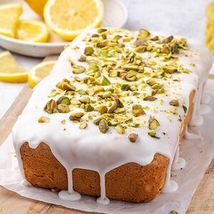 Lemon pistachio pound cake drizzled with lemon icing and decorated with crushed pistachios on a wooden board.
