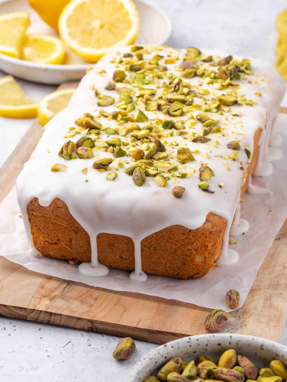 Lemon pistachio pound cake drizzled with lemon icing and decorated with crushed pistachios on a wooden board.