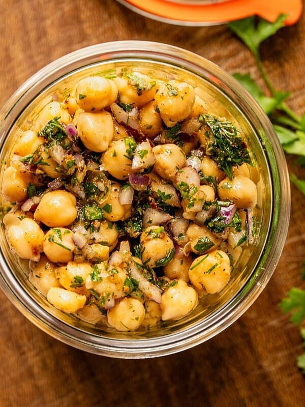 Marinated chickpeas in a mason jar with herbs, oil and seasoning sitting on a wooden board.