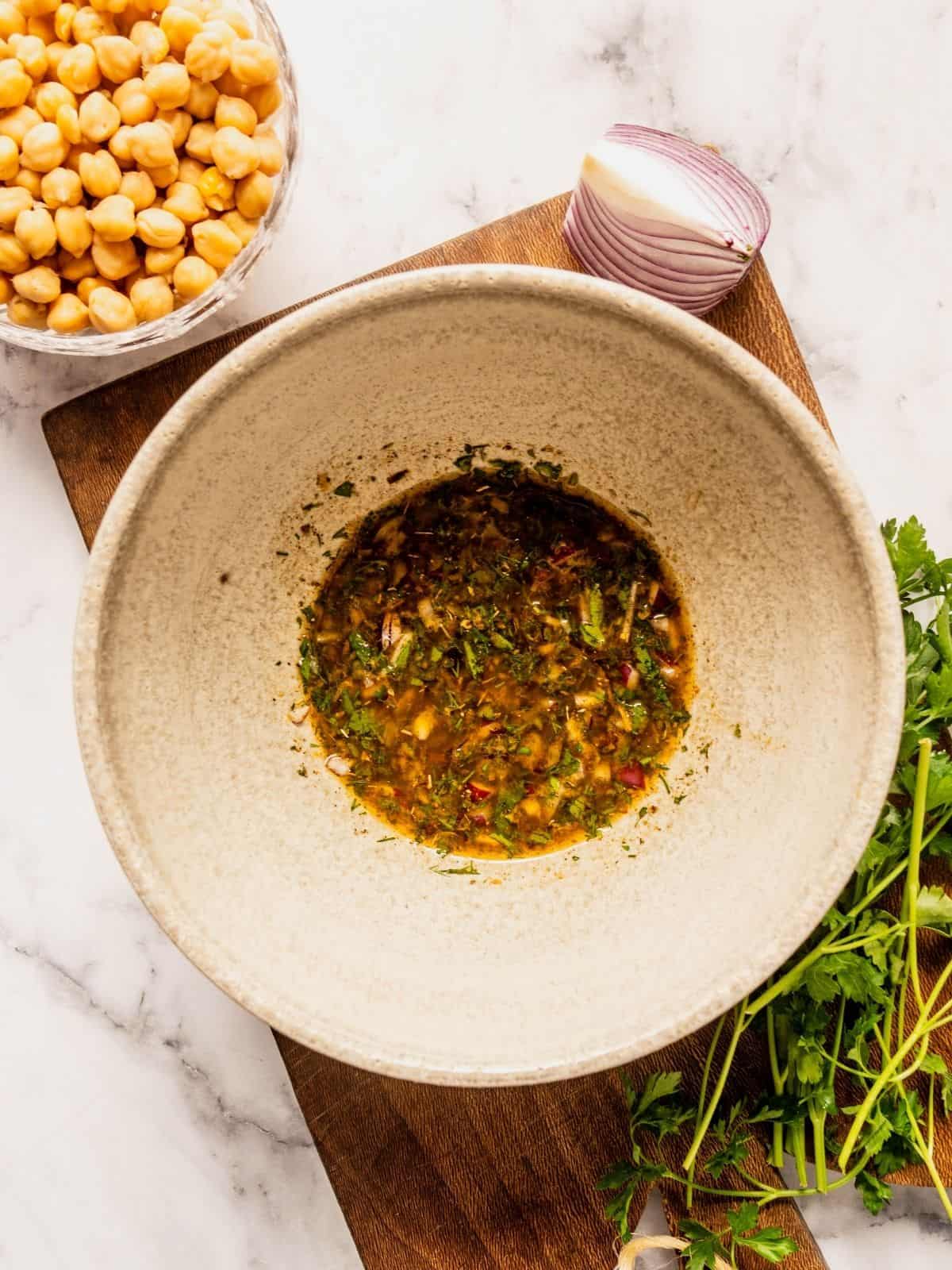 Bowl with olive oil, seasoning and herbs sitting on top of a wooden board.