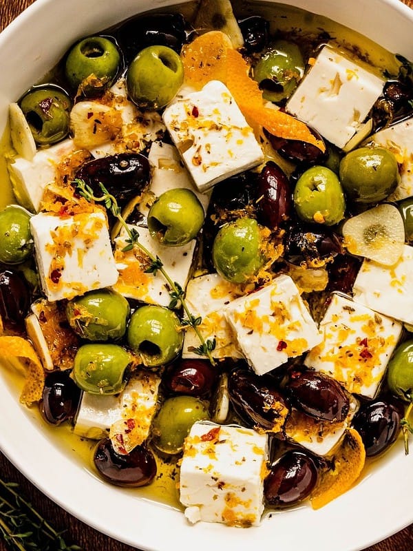 Citrus and herb marinated feta and olives in a bowl with thyme, orange peels, and spices.