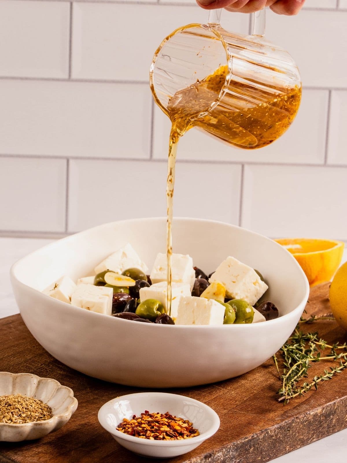 Pouring marinade over the bowl of cubed feta and mixed olives.