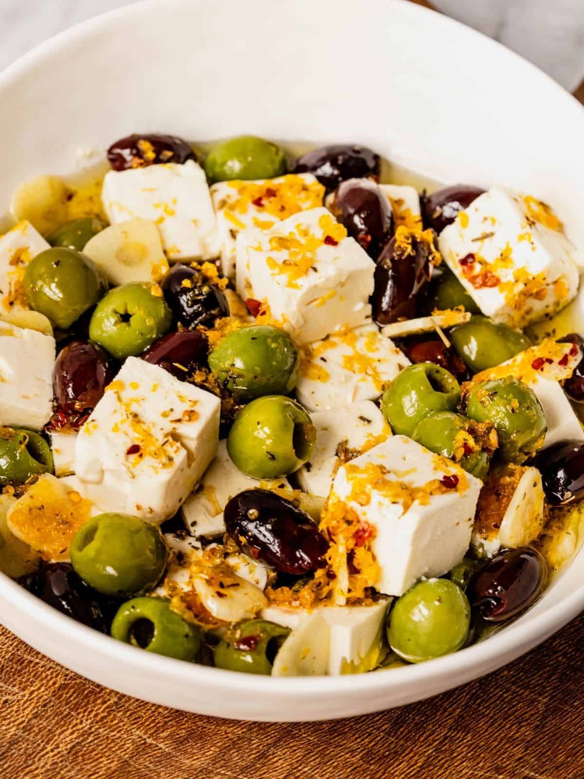 Citrus and herb marinated feta and olives in a bowl with thyme, orange peels, and spices.