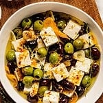 Citrus and herb marinated olives and feta in a bowl with thyme, orange peels, and spices.