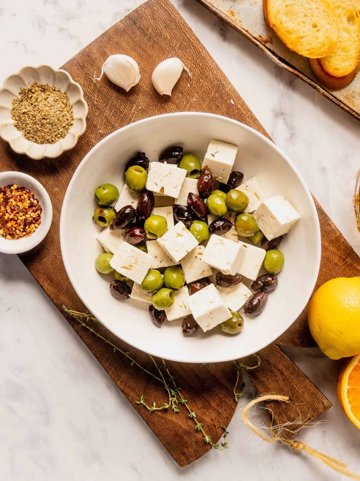 Bowl of cubed feta cheese and mixed olives on a wooden board.