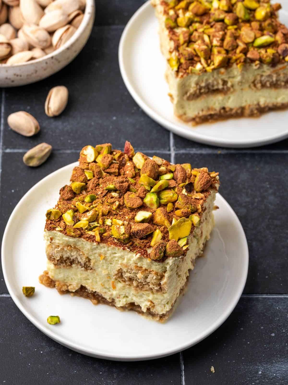 A slice of orange pistachio tiramisu decorated with crushed pistachios and cocoa on a plate.