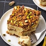 A slice of orange pistachio tiramisu decorated with crushed pistachios and cocoa on a plate.