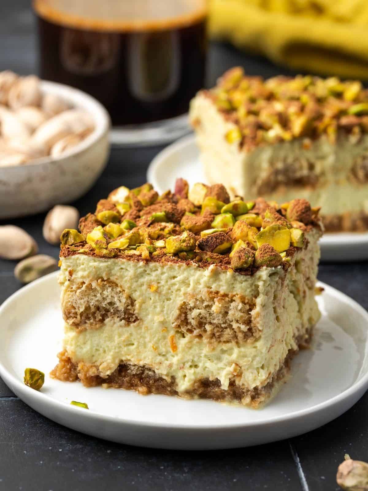 A slice of orange pistachio tiramisu decorated with crushed pistachios and cocoa on a plate.