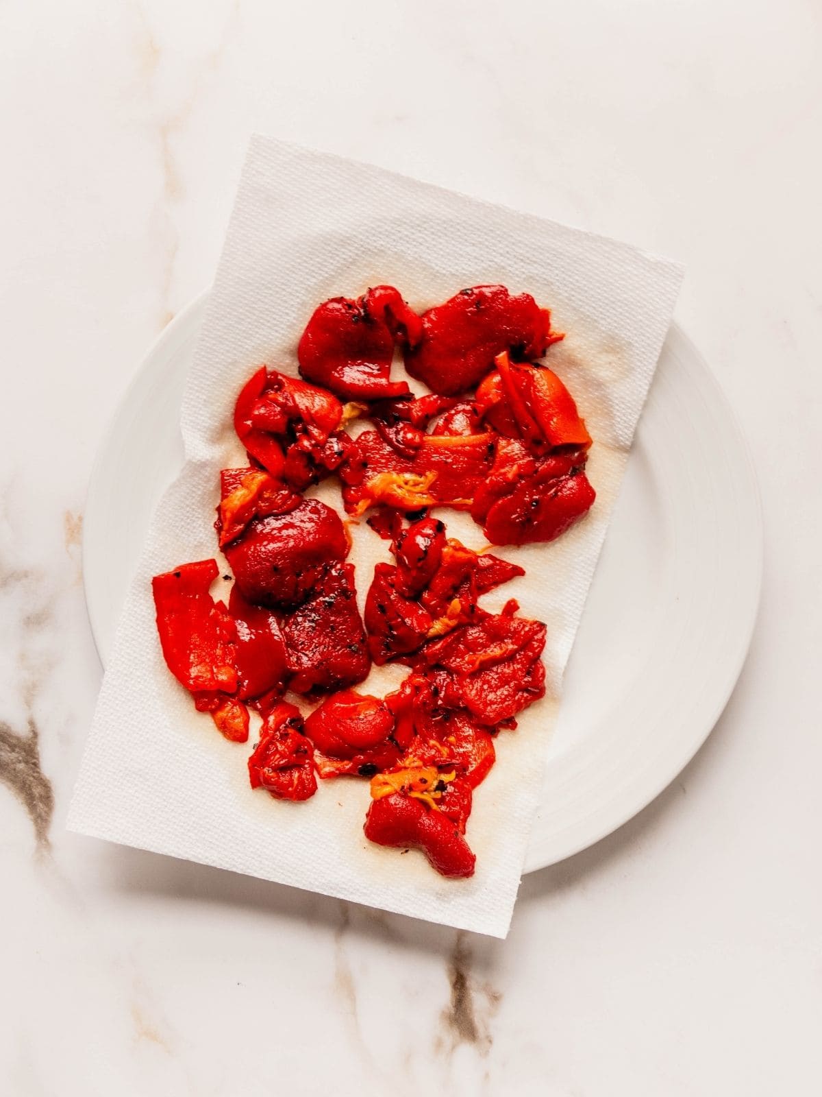 Roasted red pepper slices draining on a piece of paper towel on a plate.