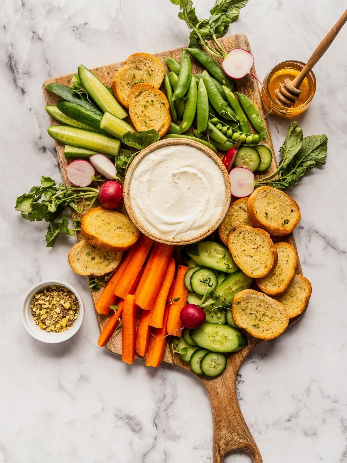 Whipped feta a bowl surrounded by pita and sliced vegetables.