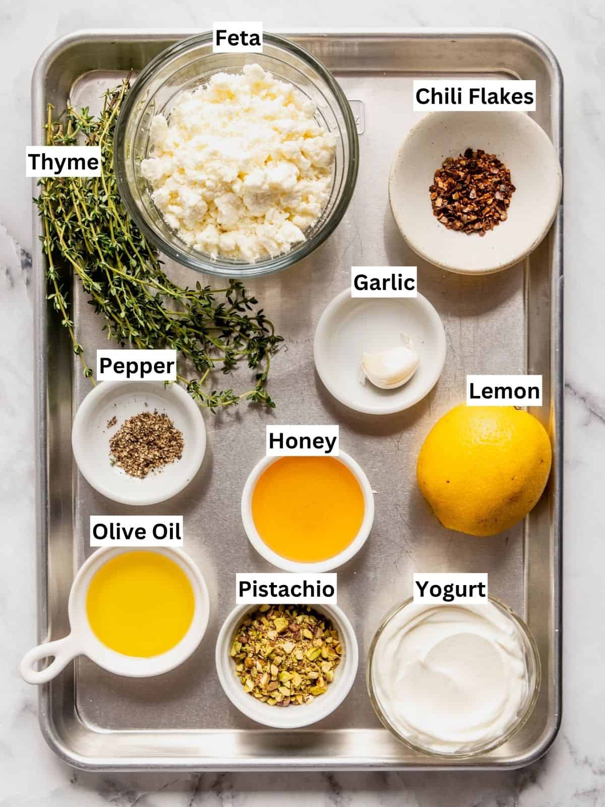 Whipped feta with honey and pistachios recipe ingredients with individual labels on a metal tray.