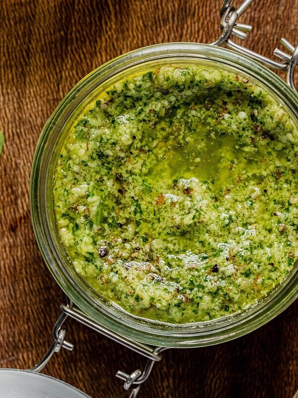 Arugula pesto in a class jar on a wooden tray.