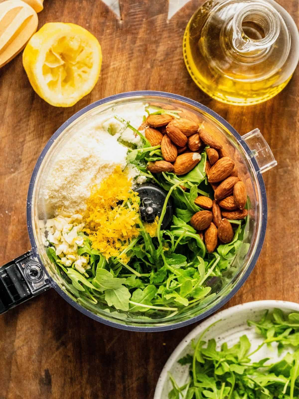 Food processor with arugula, almonds, parmesan, lemon zest, juice and garlic.