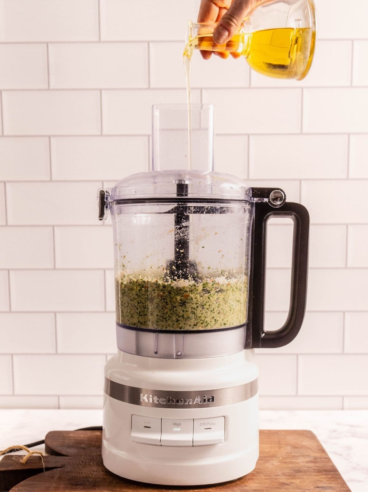 Drizzling olive oil into a food processor while it's processing the pesto.