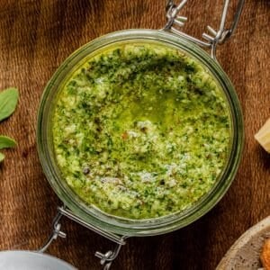 A jar of green pesto on a wooden board.
