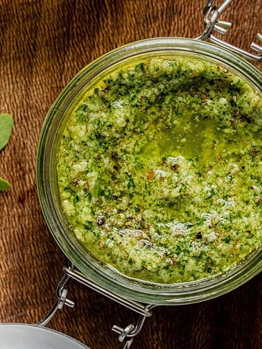 A jar of green pesto on a wooden board.