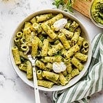 Bowl of pasta tossed with pea pesto and garnished with pea shoots, dollops of cream and cheese.