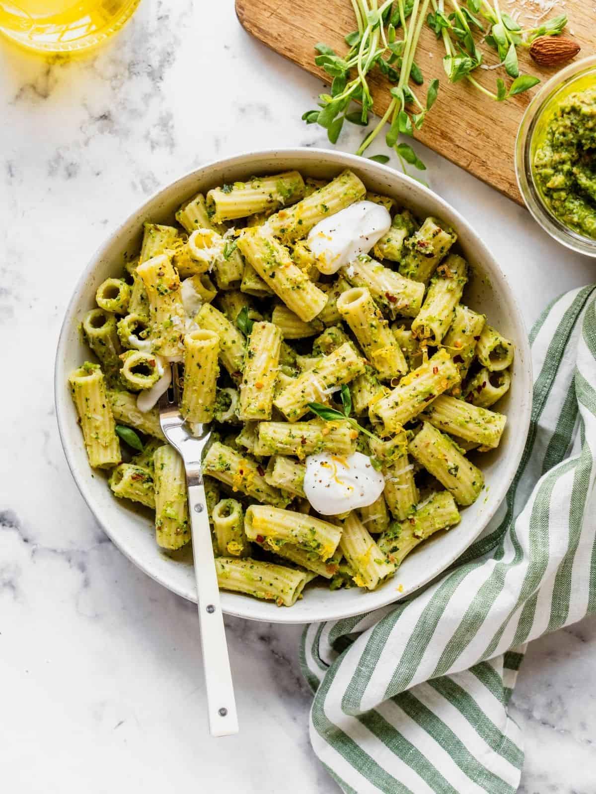 Bowl of pasta tossed with pea pesto and garnished with pea shoots, dollops of cream and cheese.