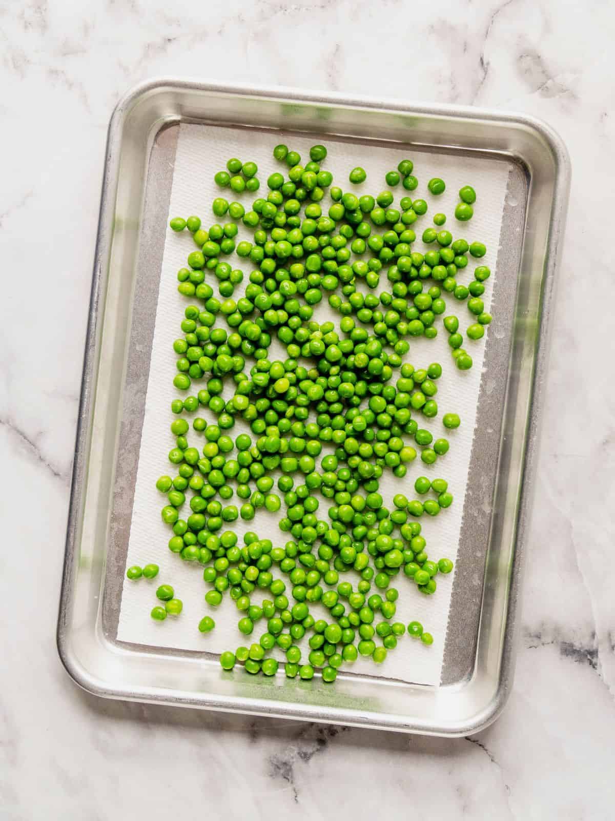 Paper-lined baking sheet with peas draining.