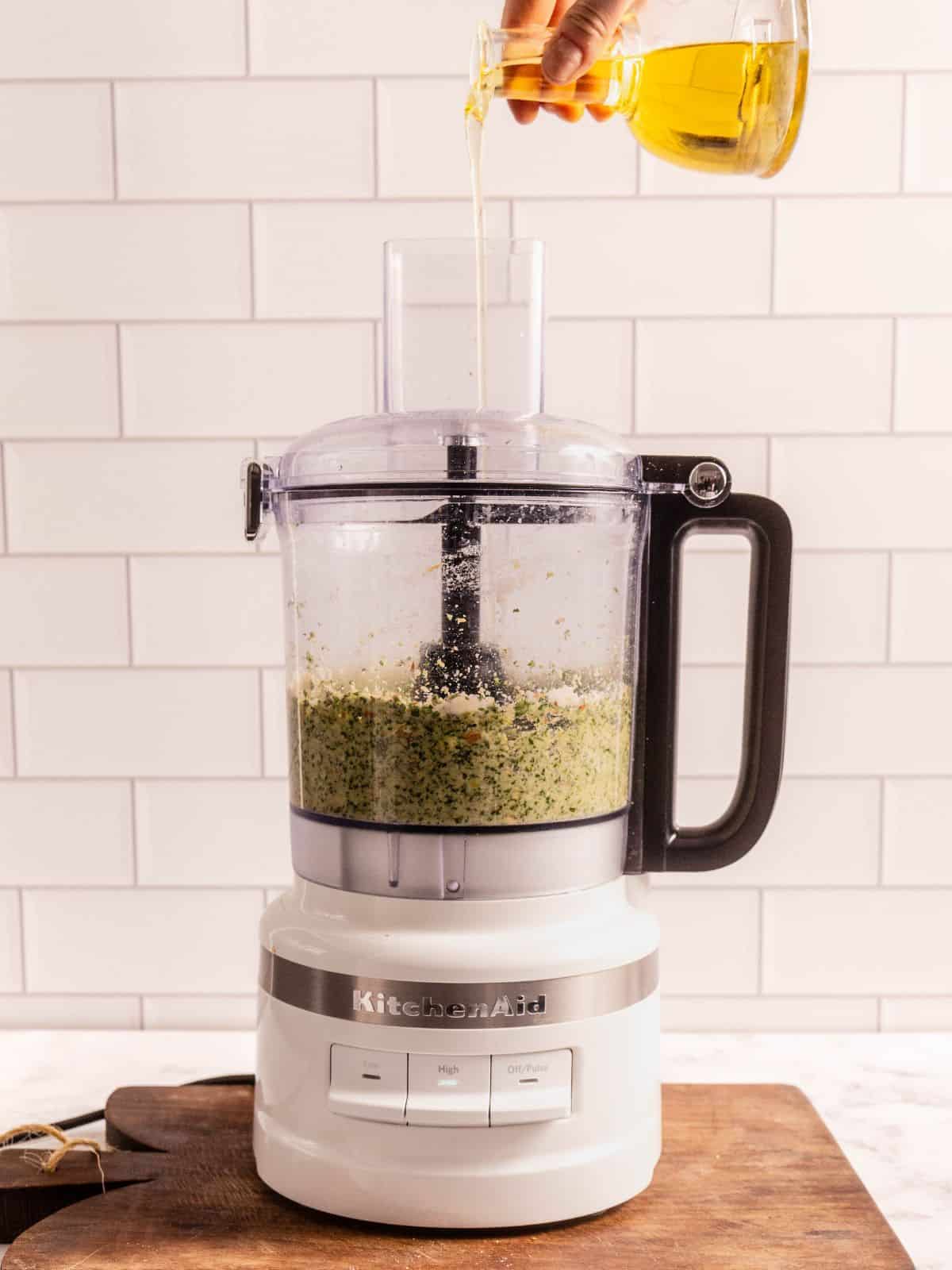 Drizzling olive oil into the food processor as it processes the pesto.