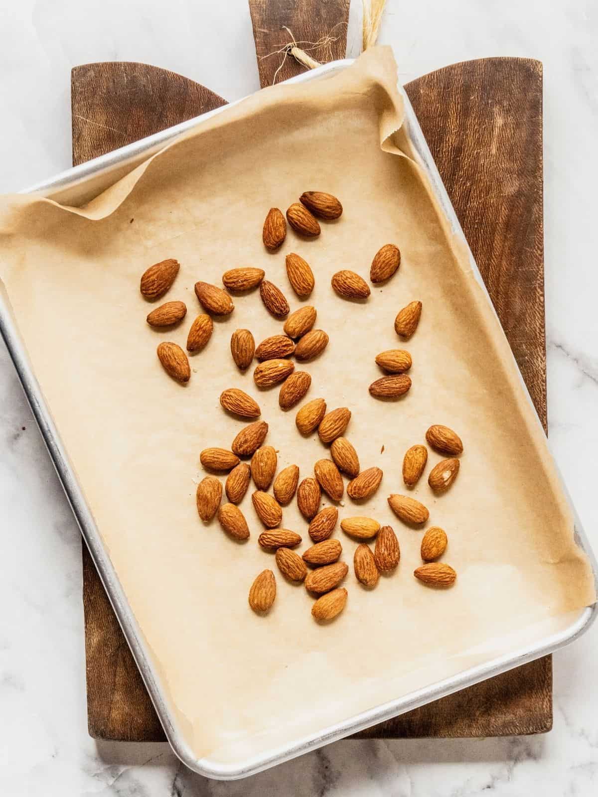 Parchment paper lined baking tray with almonds on it.