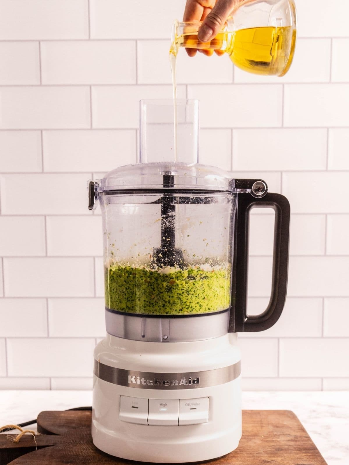 Drizzling olive oil into the food processor as it processes the pesto.