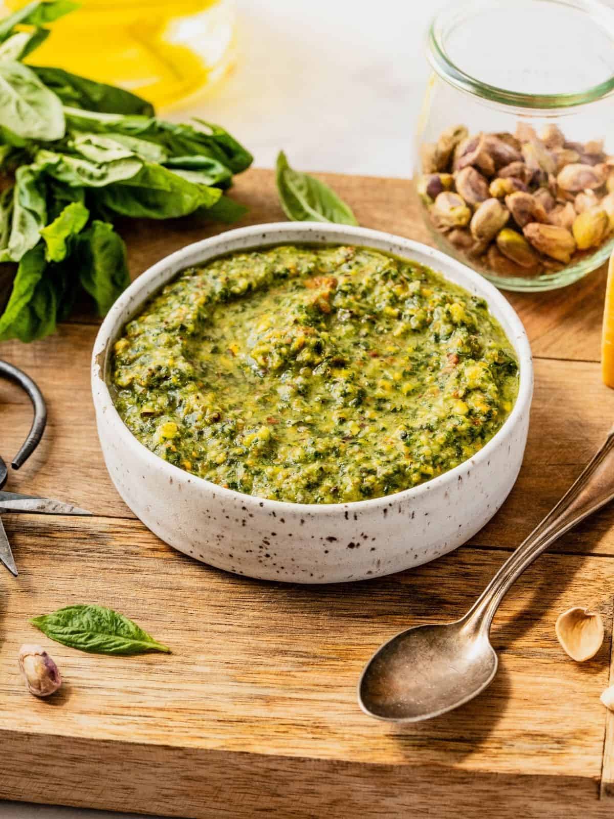 Pistachio pesto in a bowl set on top of a wooden board.