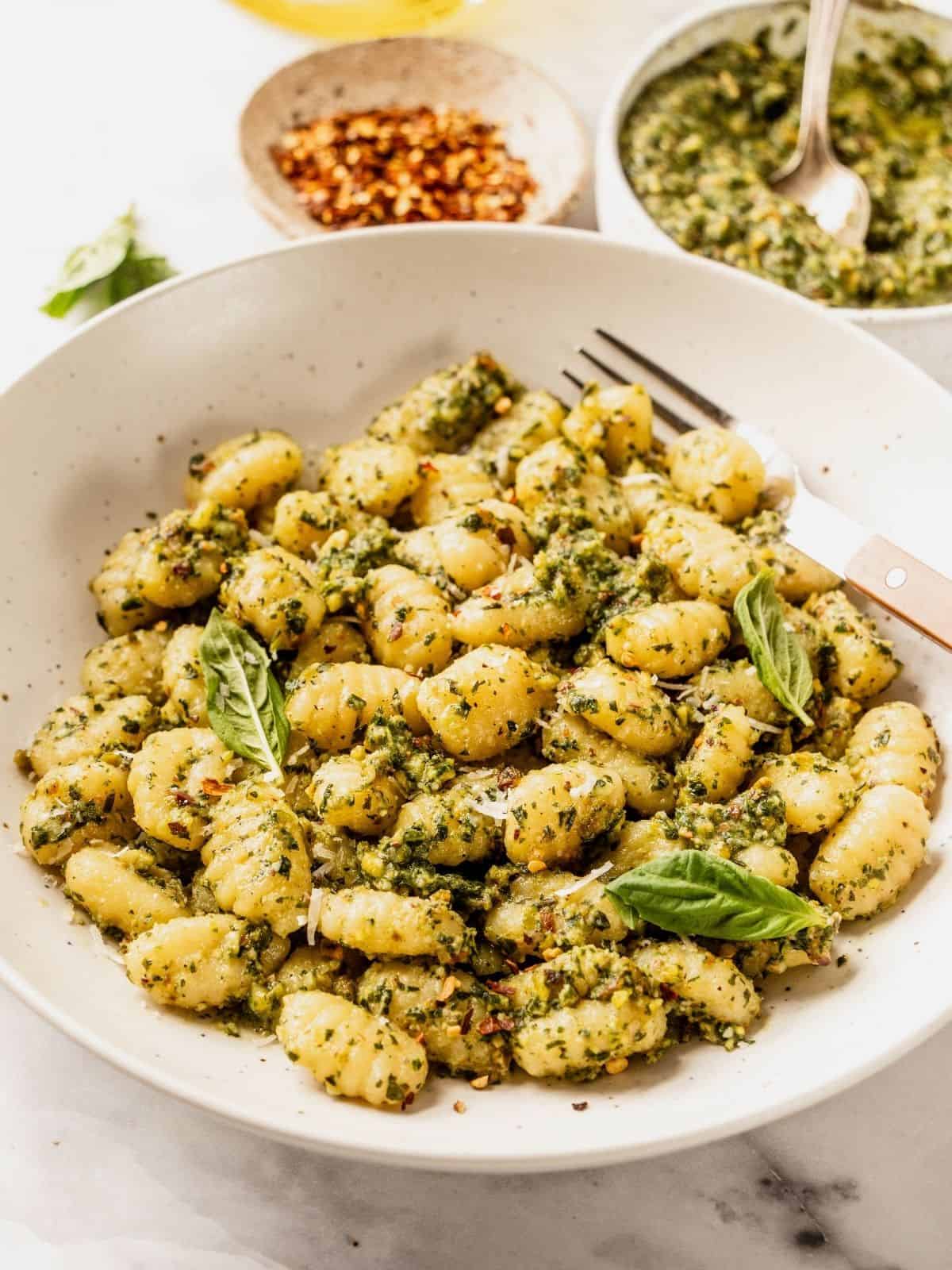 Gnocchi tossed with pistachio pesto and garnished with fresh basil in a bowl.