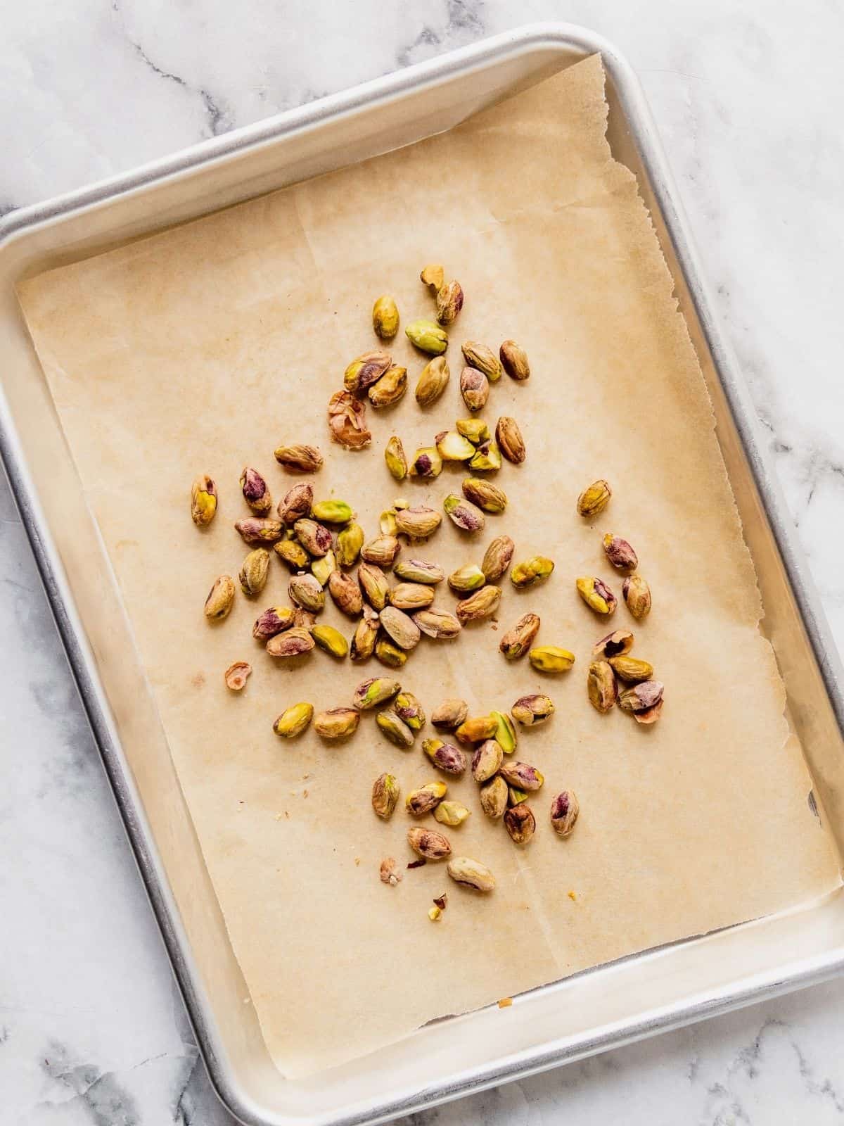 Parchment paper lined baking sheet with pistachios.
