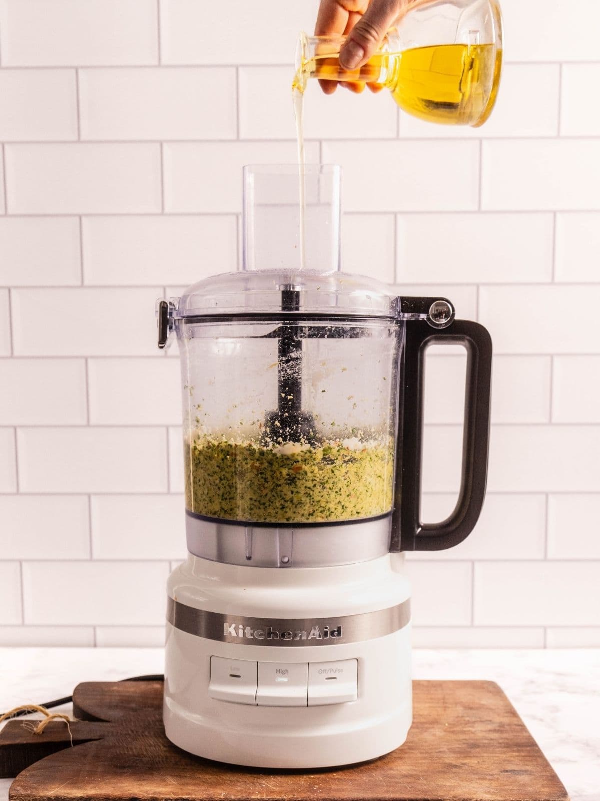 Drizzling oil into the food processor as it runs.