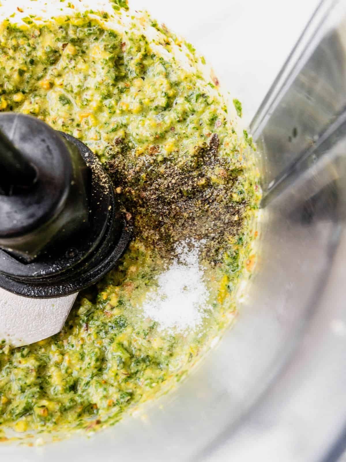 Seasoning the pistachio pesto with salt and pepper in a food processor.