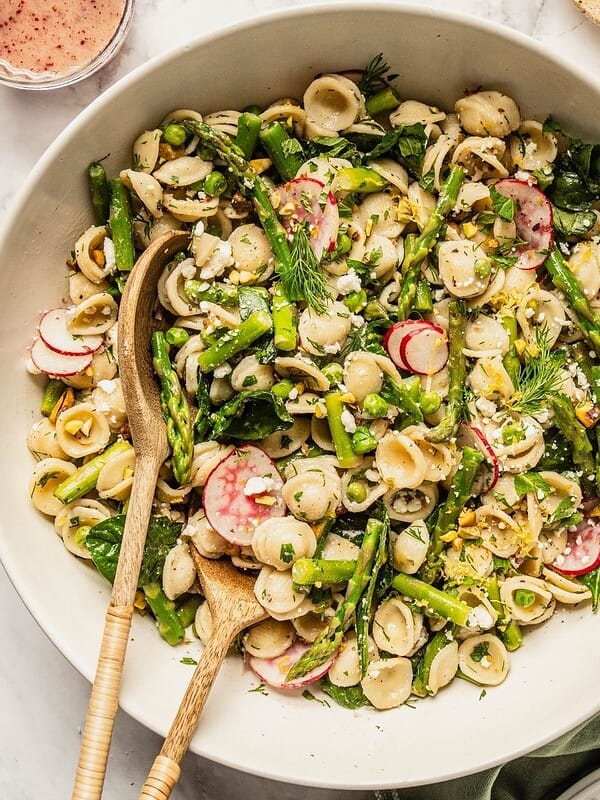 Bowl of spring pasta salad loaded with asparagus, radish, spinach, herbs and a tangy sumac honey dressing.