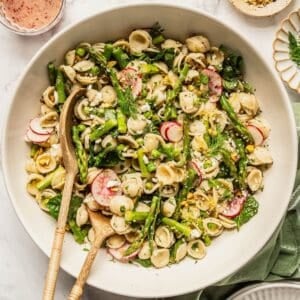 Spring pasta salad with asparagus and peas in a bowl with salad spoons.